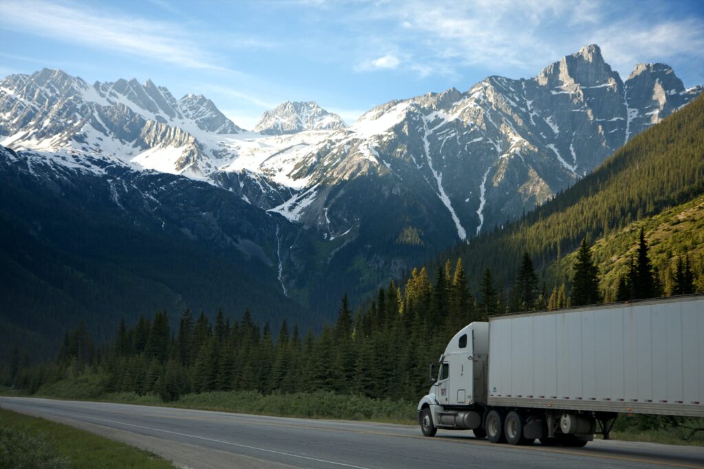 A truck driving through a clean road with trees and mountains in the background.